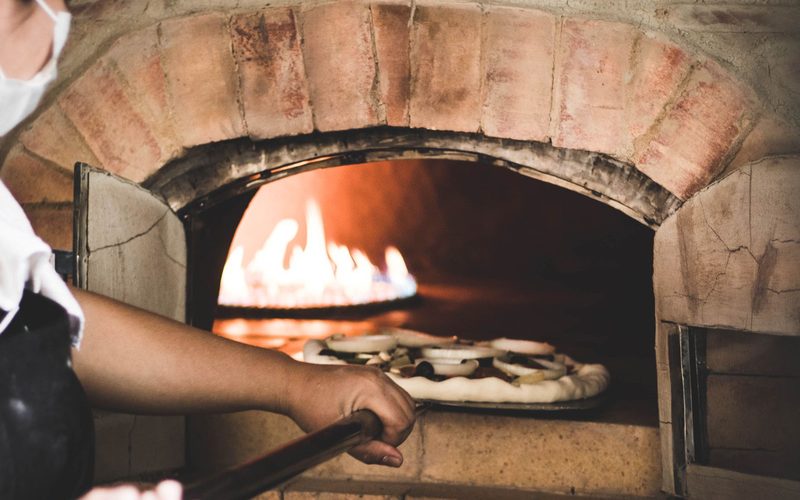 Il pizzaiolo infila una pizza nel forno a legna acceso