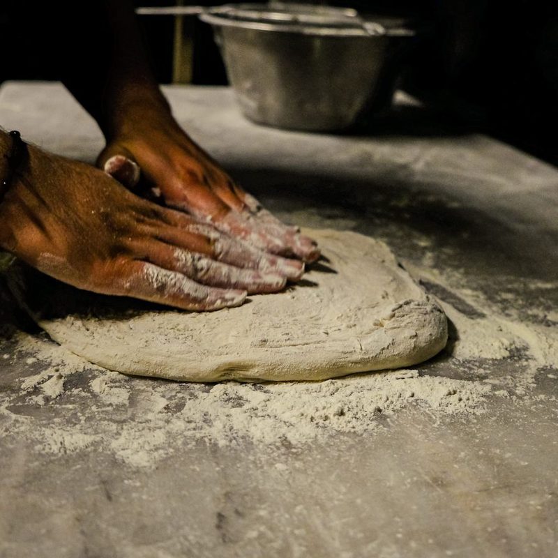 Le mani del pizzaiolo che stendono l'impasto sul banco infarinato